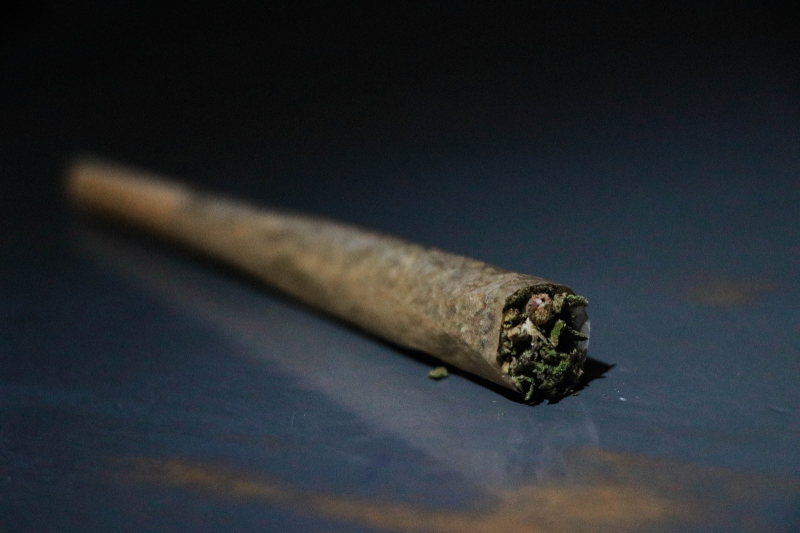 Cannabis pre-roll joint with a cone tip resting on a dark surface