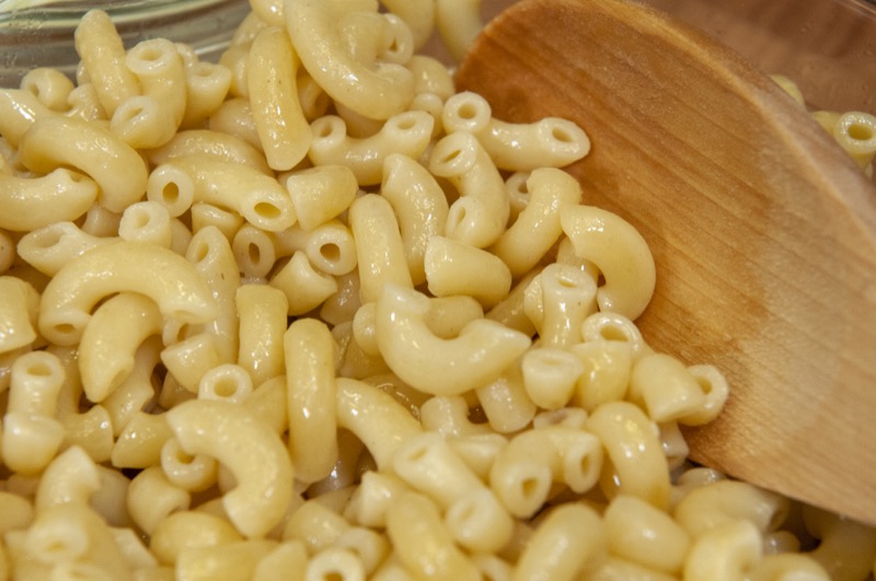 Pile of plain cooked elbow macaroni pasta drained with a wooden spoon
