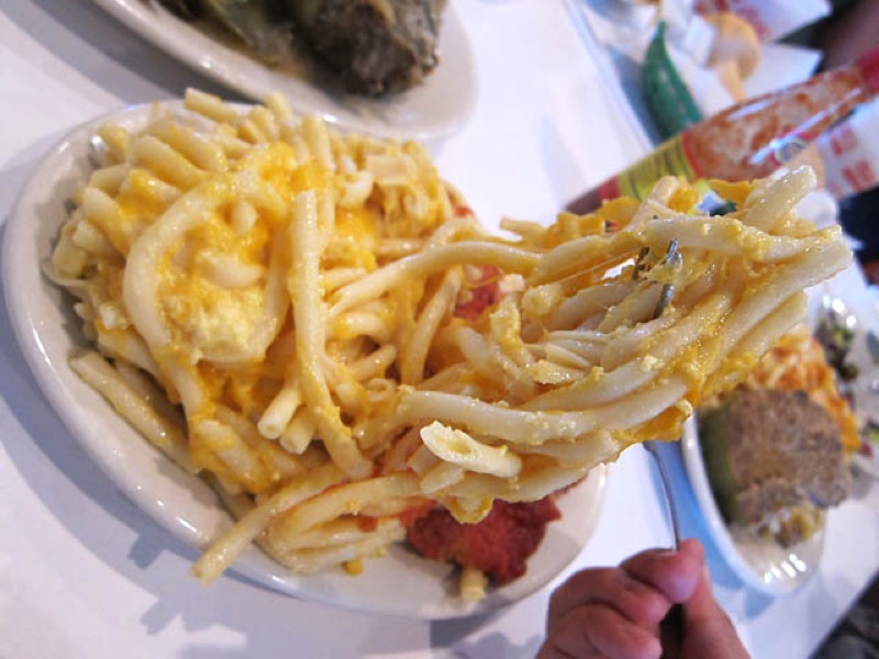 Plated serving of baked macaroni and cheese on a white plate with cheddar pulls