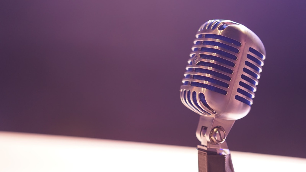 Stand-up comedy microphone on a brick-wall stage under a single warm spotlight, the visual shorthand for the modern weed-comic ecosystem.