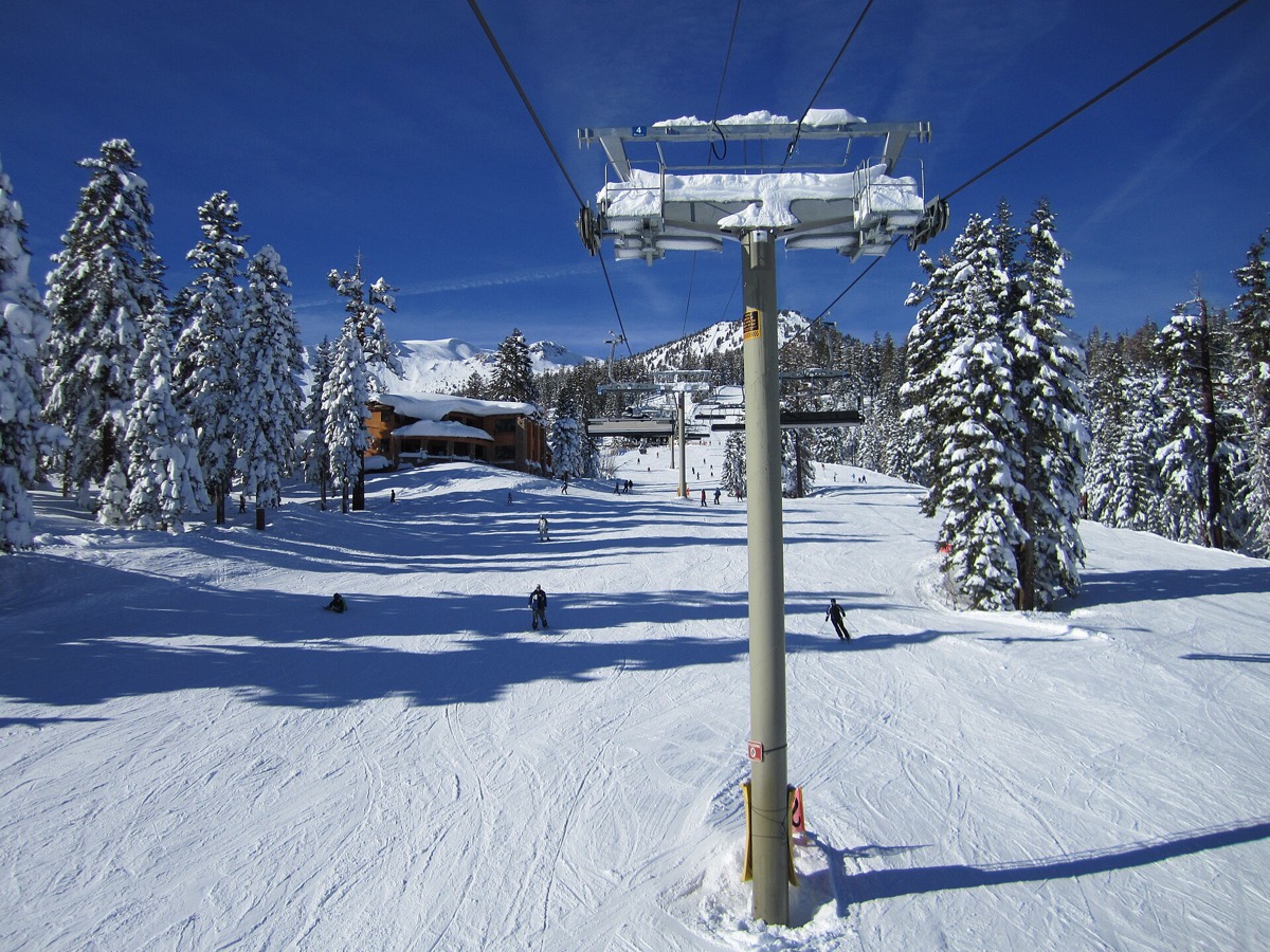 Skiers riding the Mammoth Mountain Eagle Express chairlift above snow-loaded pines on a bluebird Eastern Sierra winter day