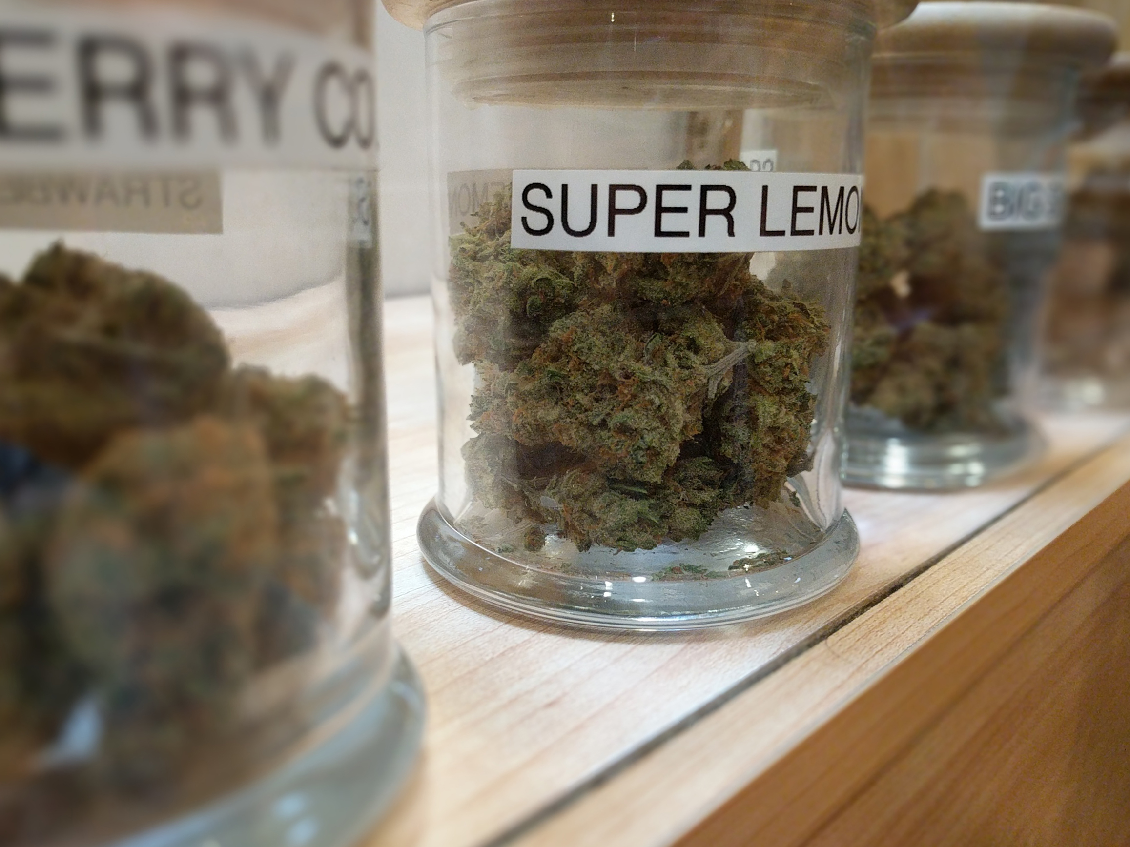 Glass jars of cured cannabis flower with strain labels lined on a wooden shelf inside a licensed adult-use dispensary, representative of the curated flower wall at Dispensary 33 Andersonville