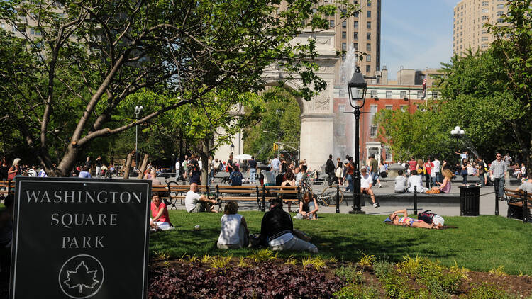 Washington Square Park arch and fountain in Greenwich Village, Manhattan, with people relaxing on benches and grass