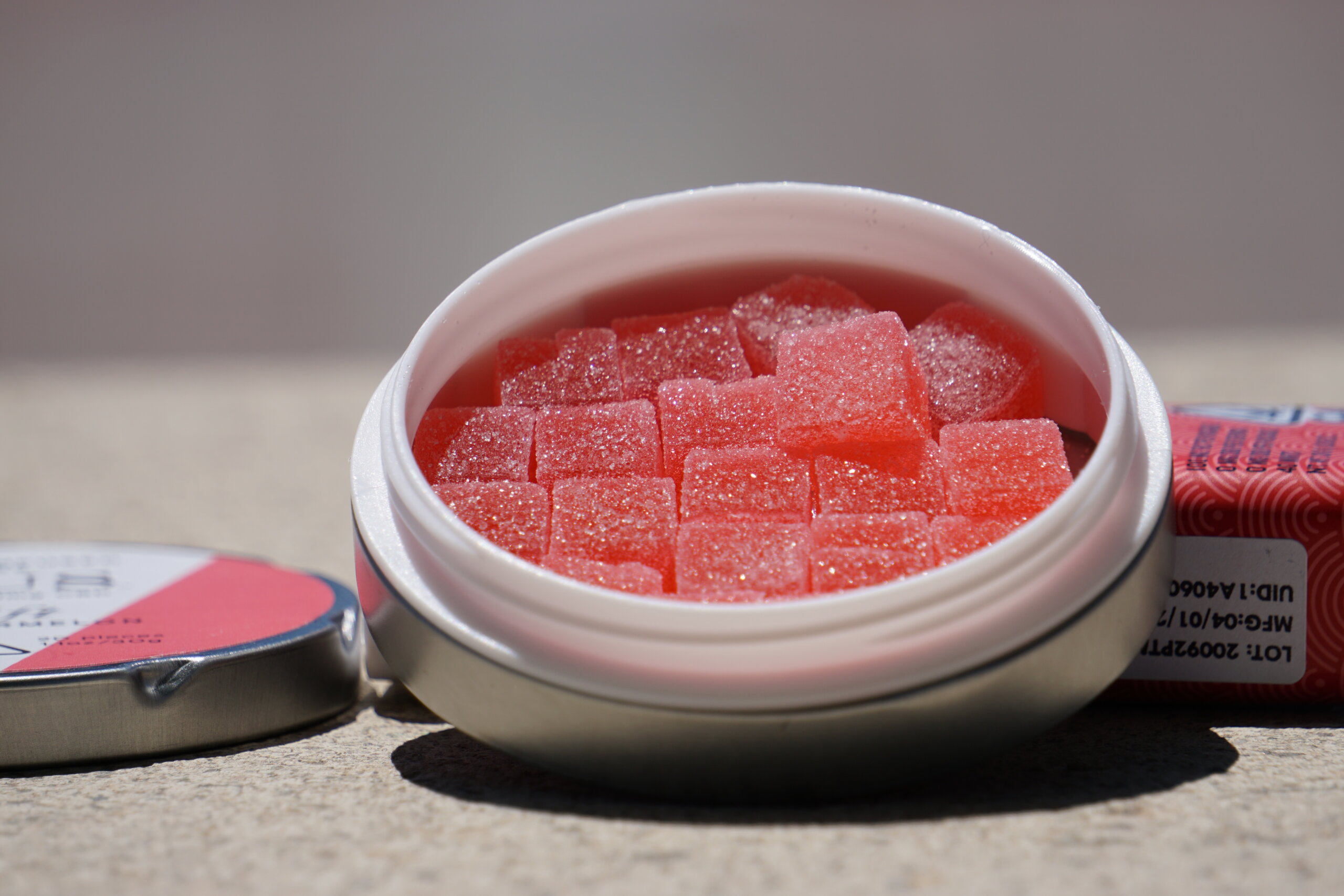 Sugar-coated cannabis sativa gummies in an open metal tin on a sunlit concrete surface, representative of the regulated edible category Verano produces under its Encore brand for the Illinois market